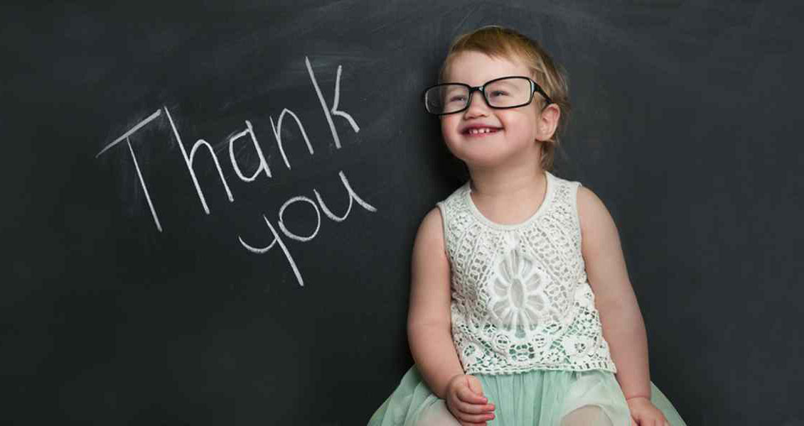 young girl wearing glasses standing in front of a blackboard with the words "Thank You" written on it